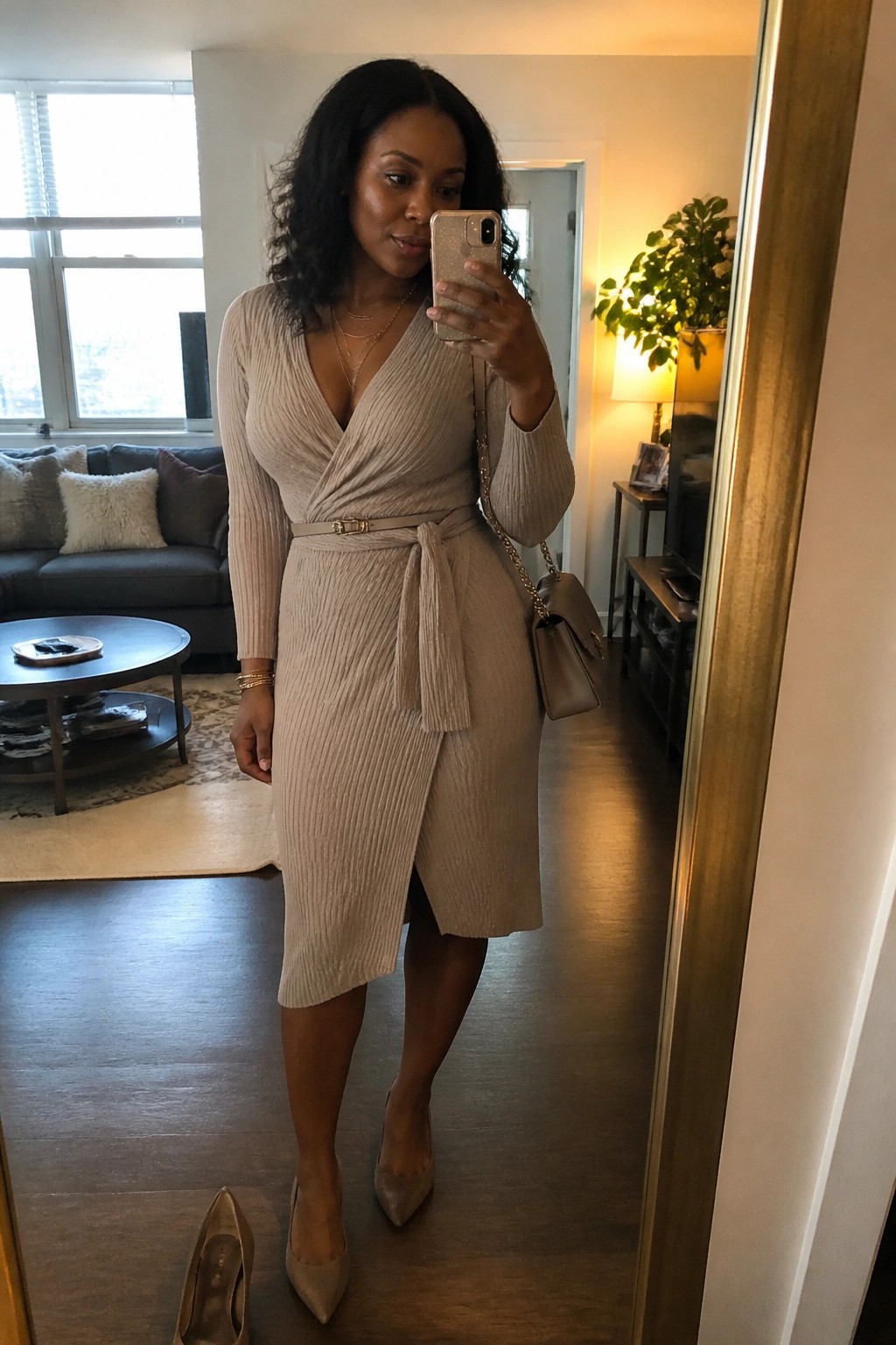 Woman in beige ribbed wrap dress taking mirror selfie in modern living room