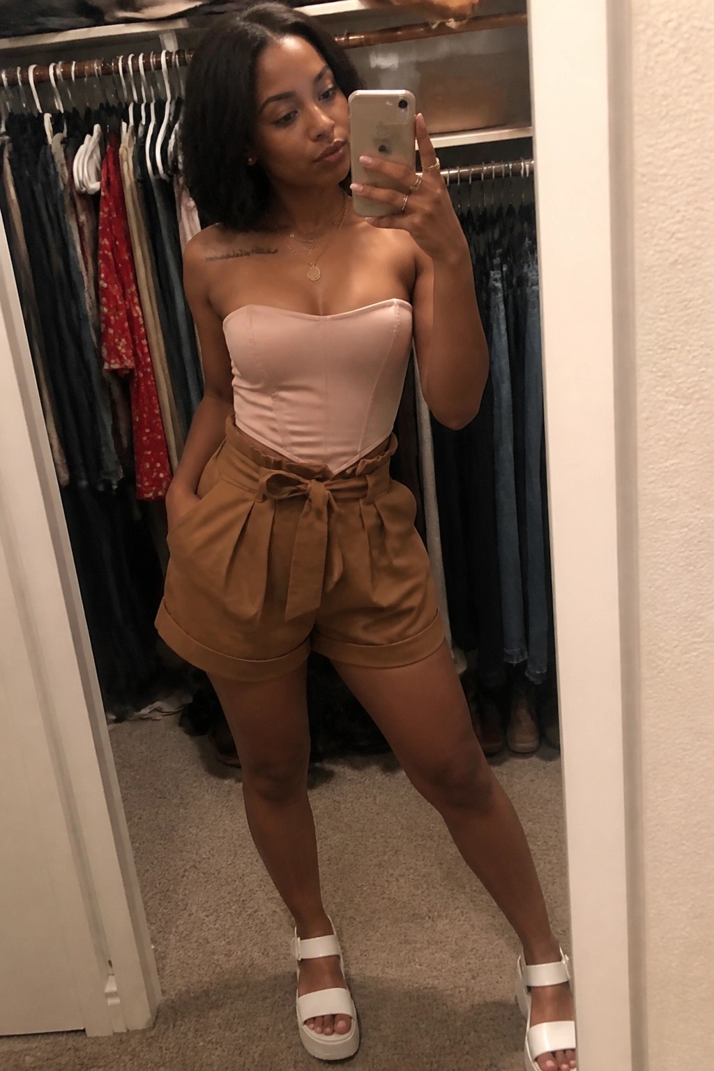 Woman in pink strapless top and brown shorts taking mirror selfie in closet