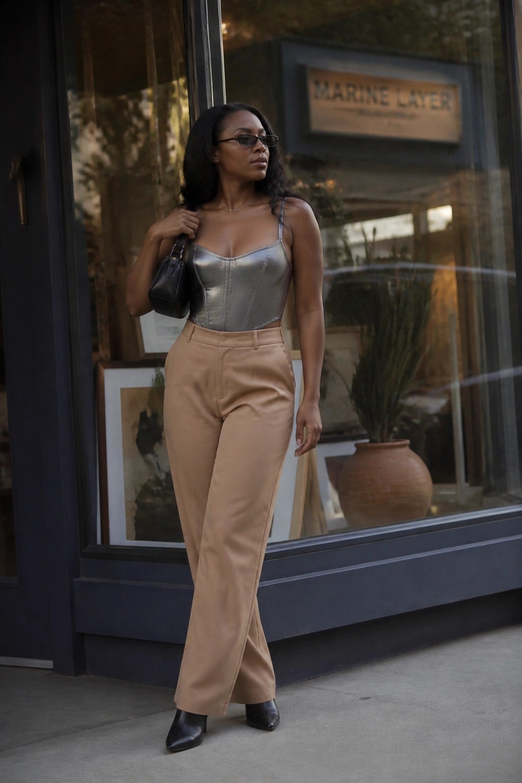Woman in metallic silver corset and beige trousers posing by store window