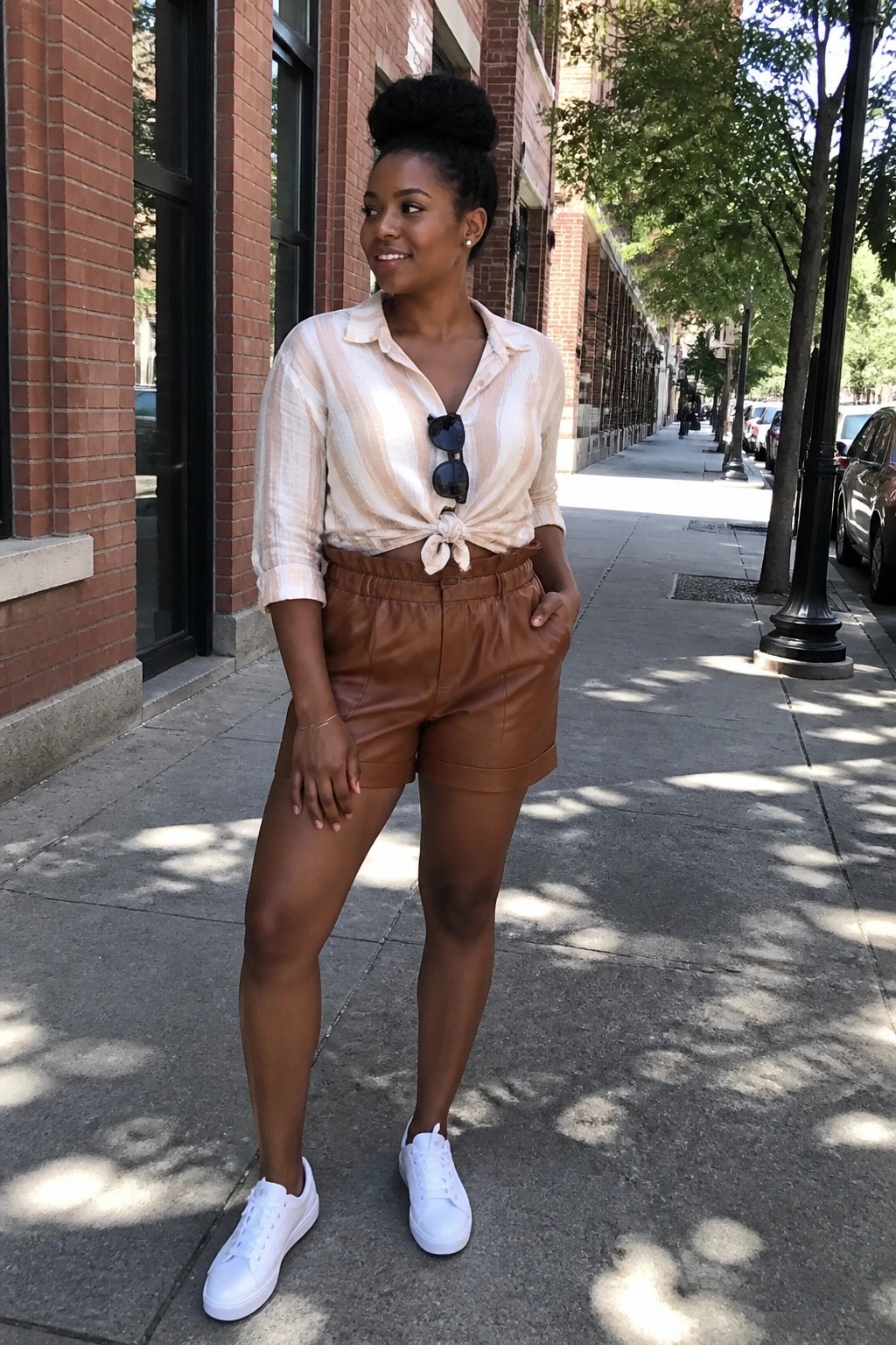 Woman in striped tied blouse and brown shorts on city sidewalk with white sneakers