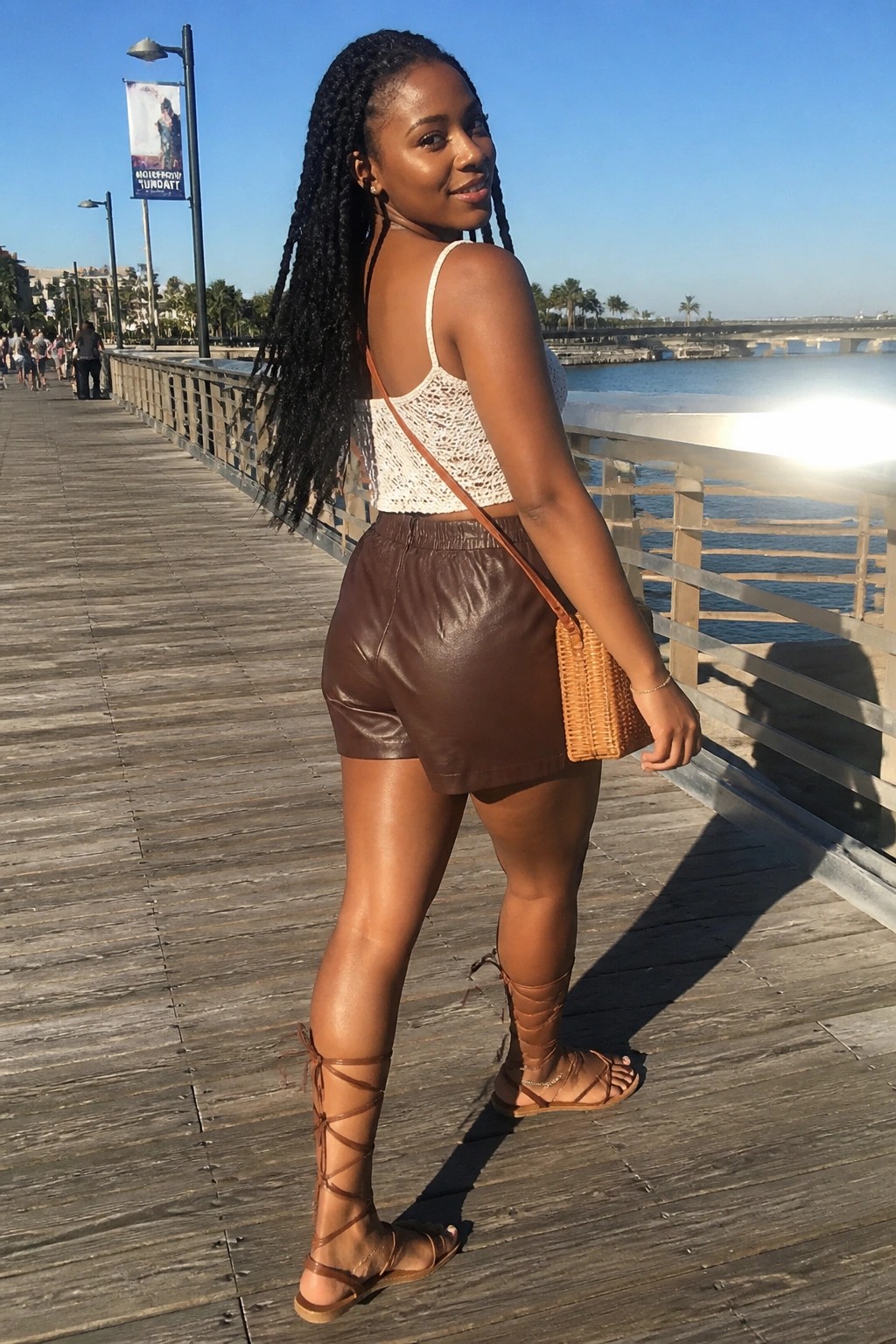 Woman with long braids in white crochet top and brown shorts on sunny pier