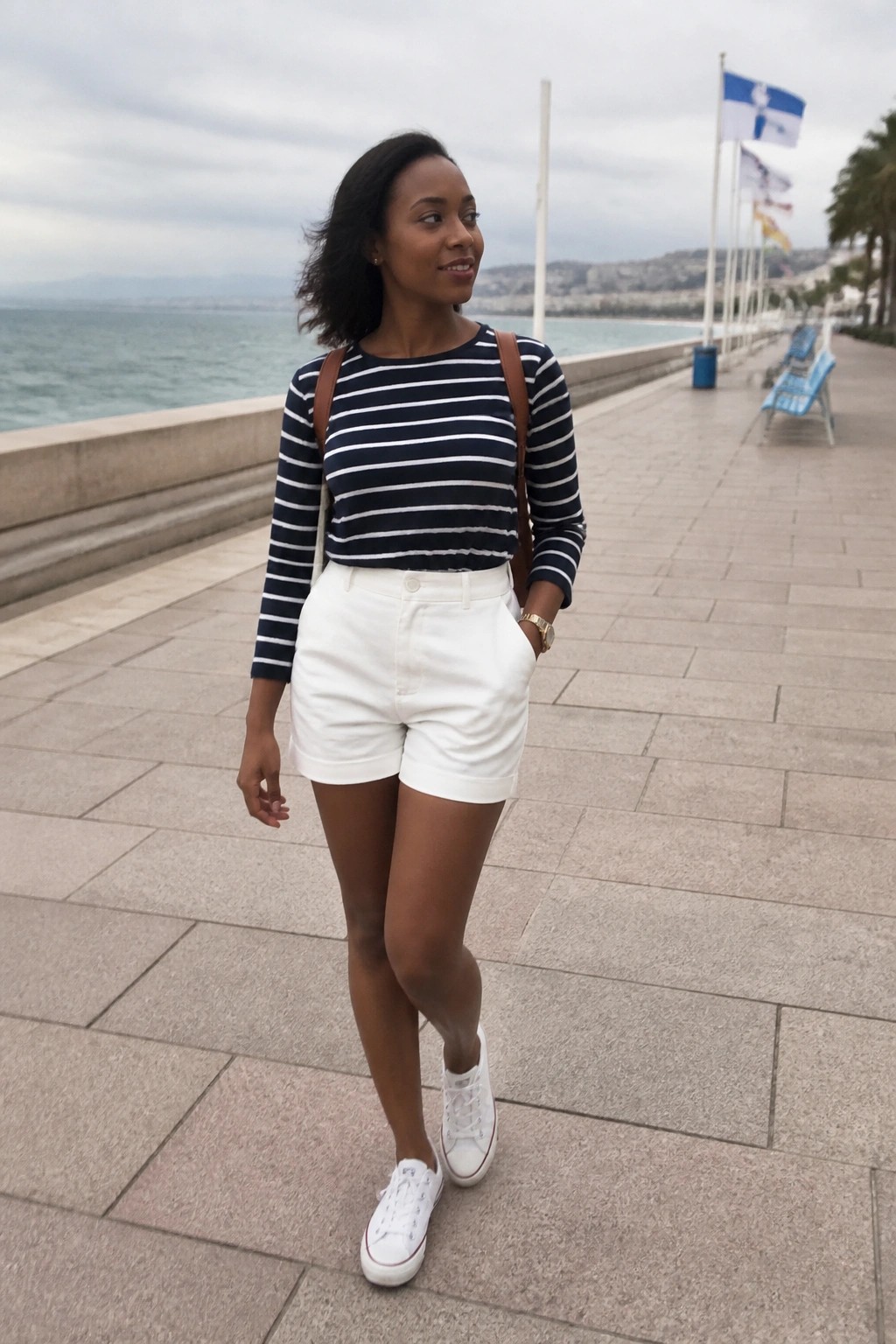 Woman in striped shirt and white shorts on seaside promenade with flags.