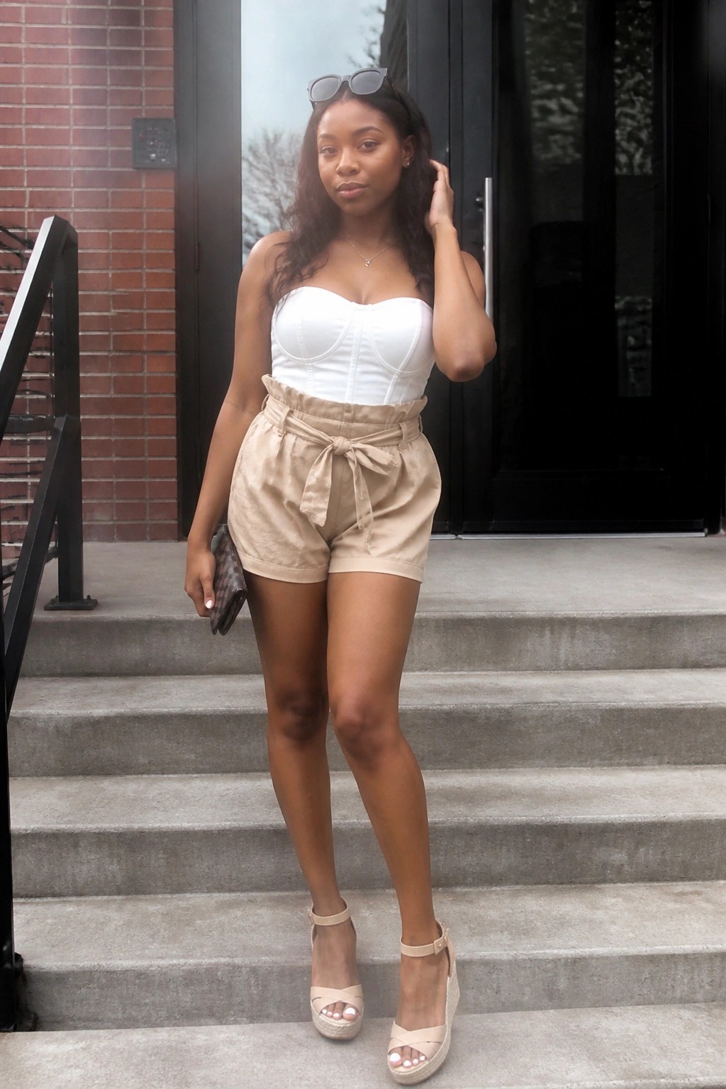 Woman in white corset top and beige tie-waist shorts with wedge sandals on steps