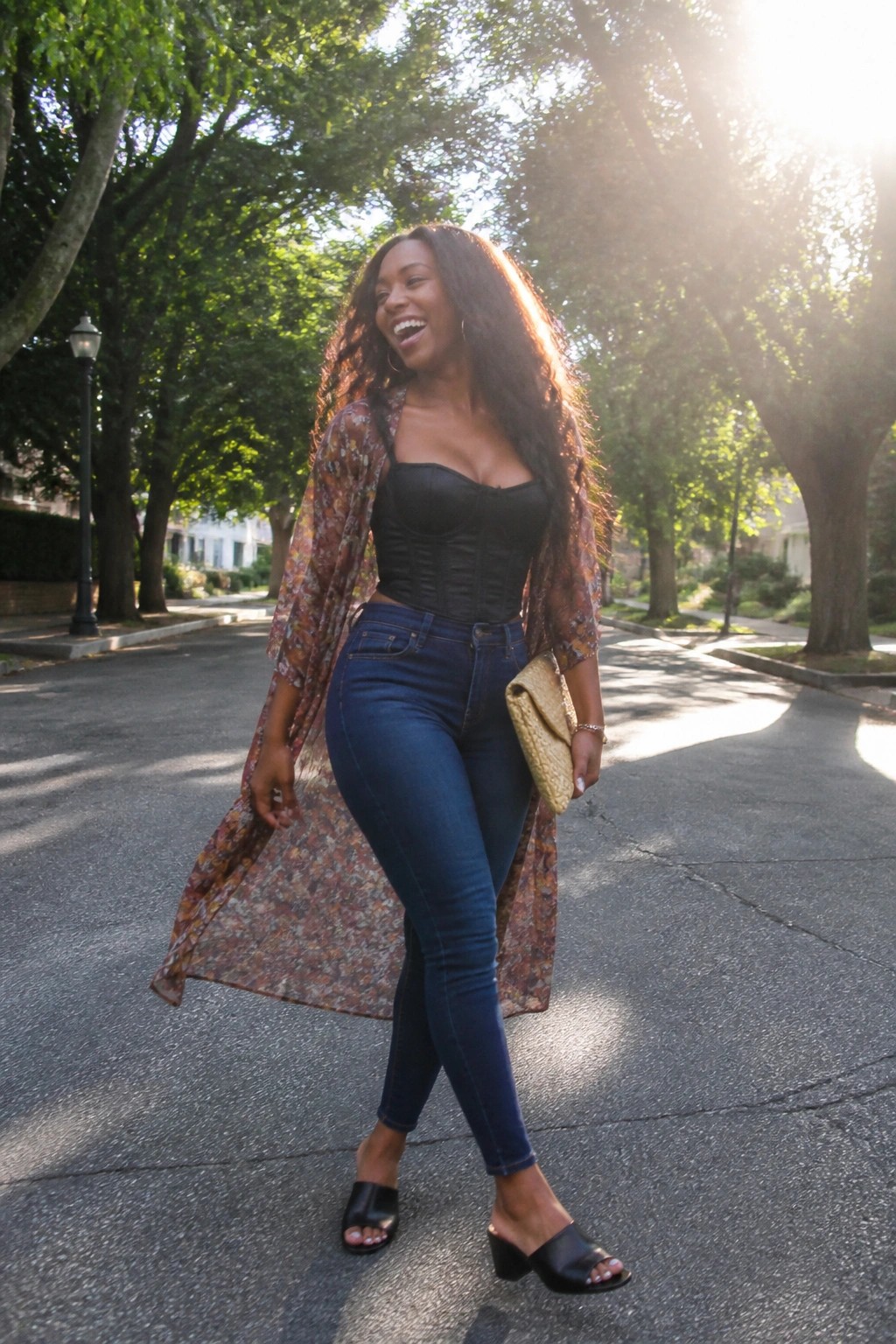 Laughing woman in floral duster over black corset on sunny tree-lined street