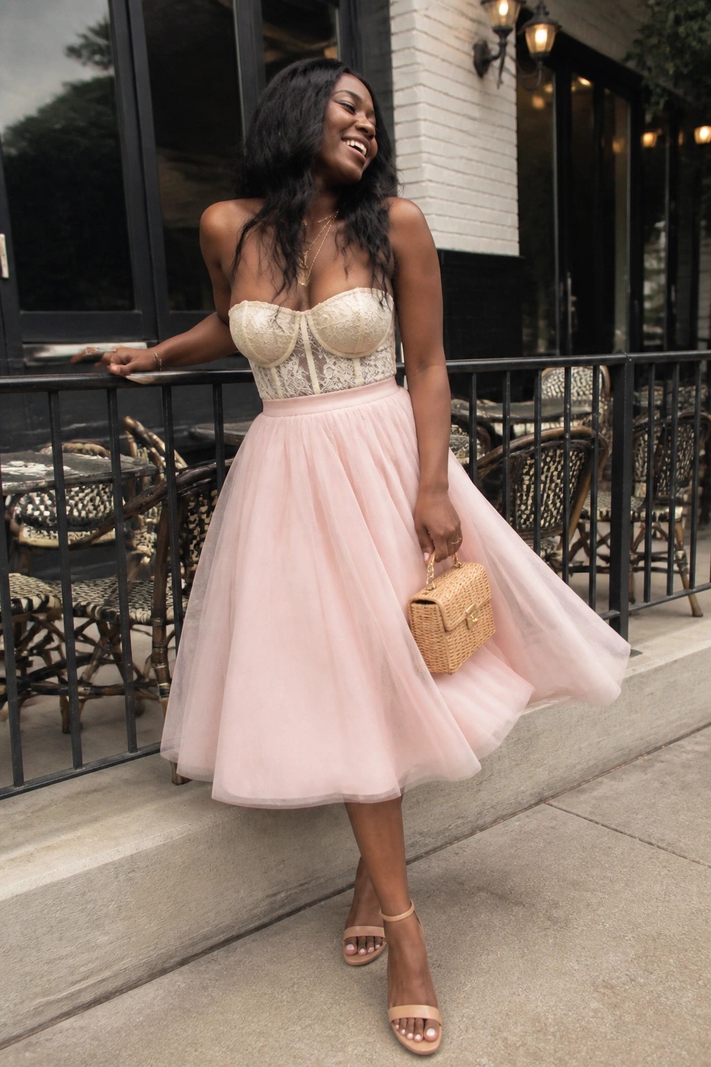 Smiling woman in pink tulle skirt and lace corset top holding woven handbag outdoors