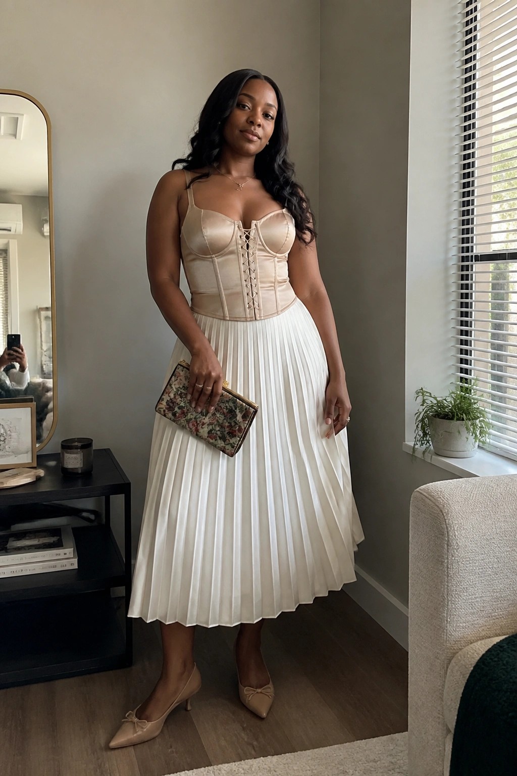 Woman in beige corset and white pleated skirt holding floral clutch in modern room
