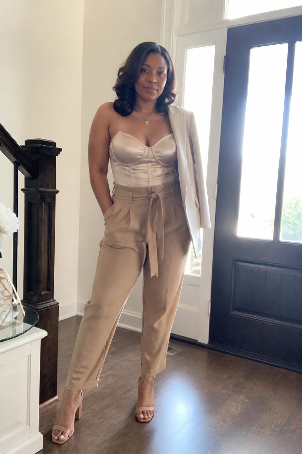 Woman in strapless beige corset, tan belted trousers, and white blazer