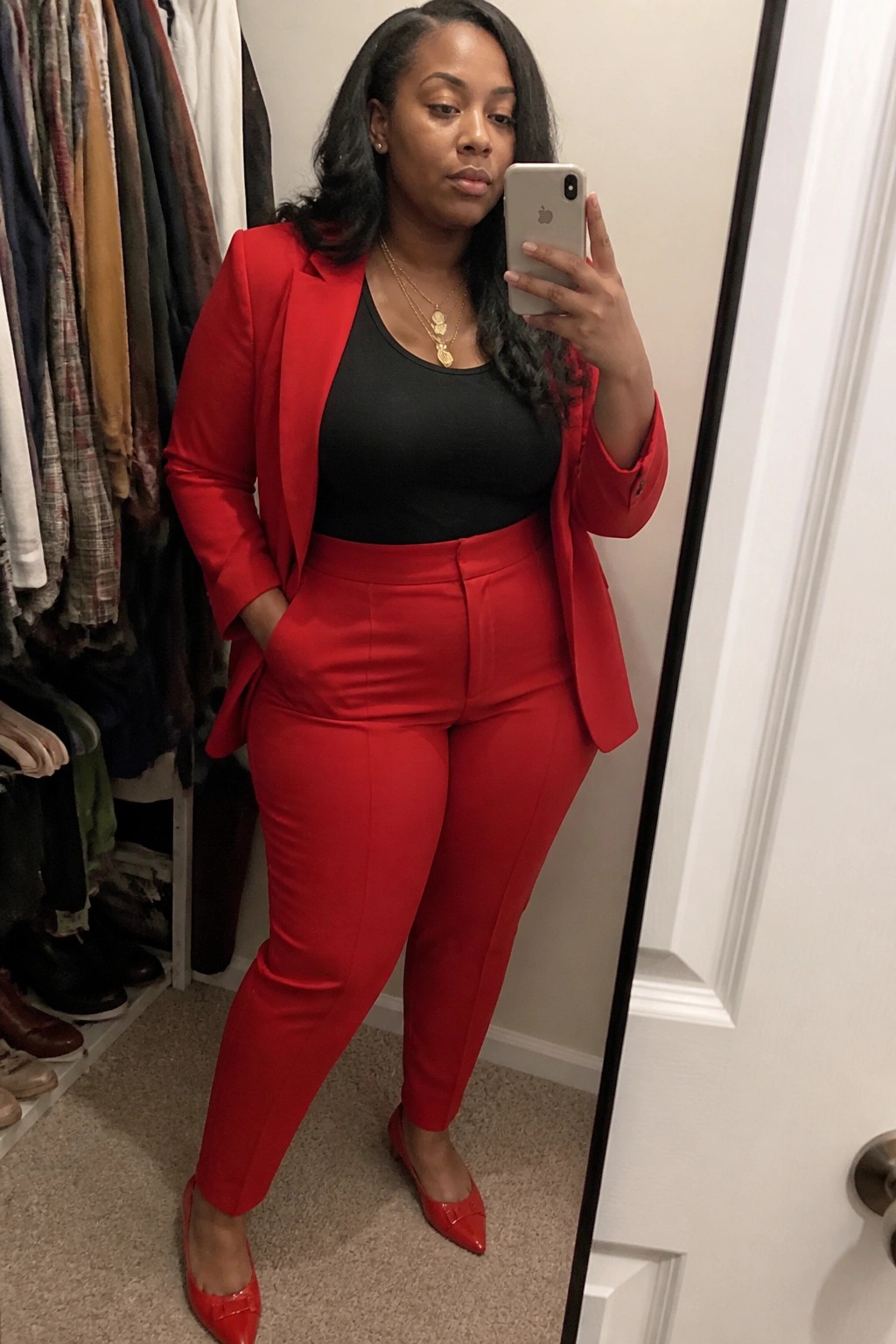 Woman in red blazer and pants taking mirror selfie in closet