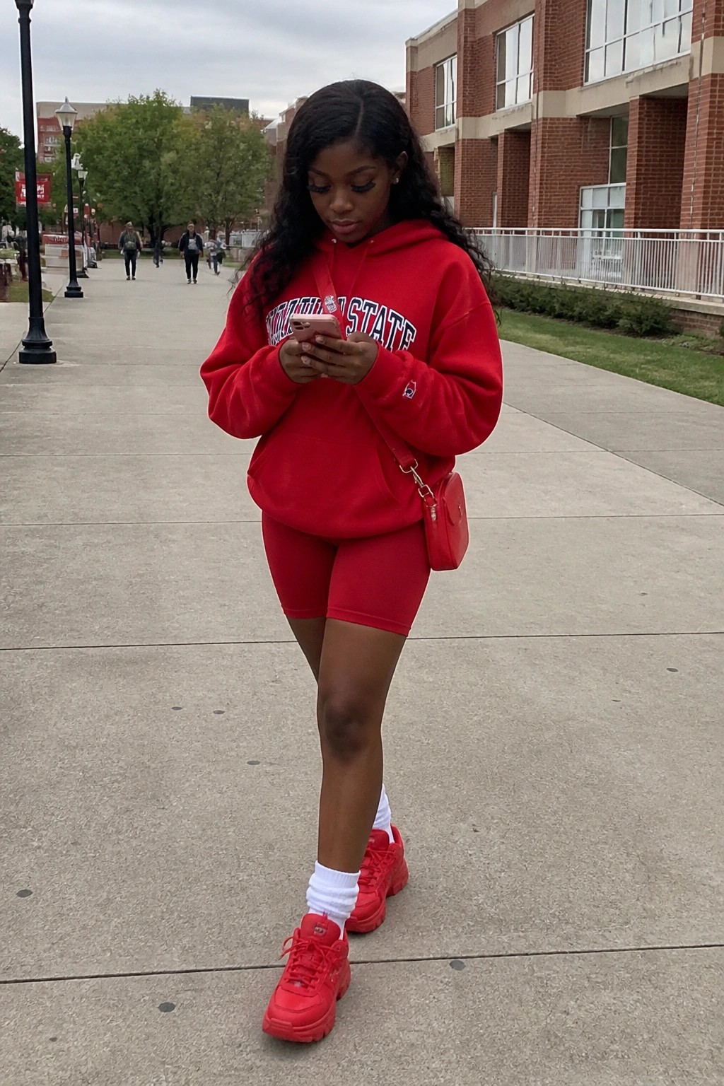 Woman in red Missouri State hoodie and shorts checks phone on walkway