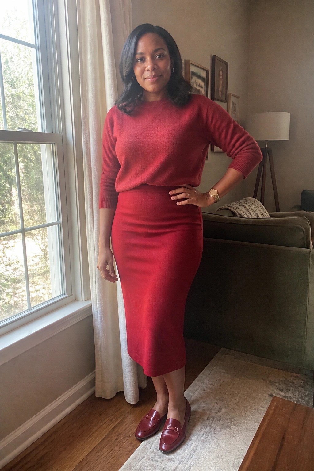 Woman in red sweater and pencil skirt posing with hand on hip in living room