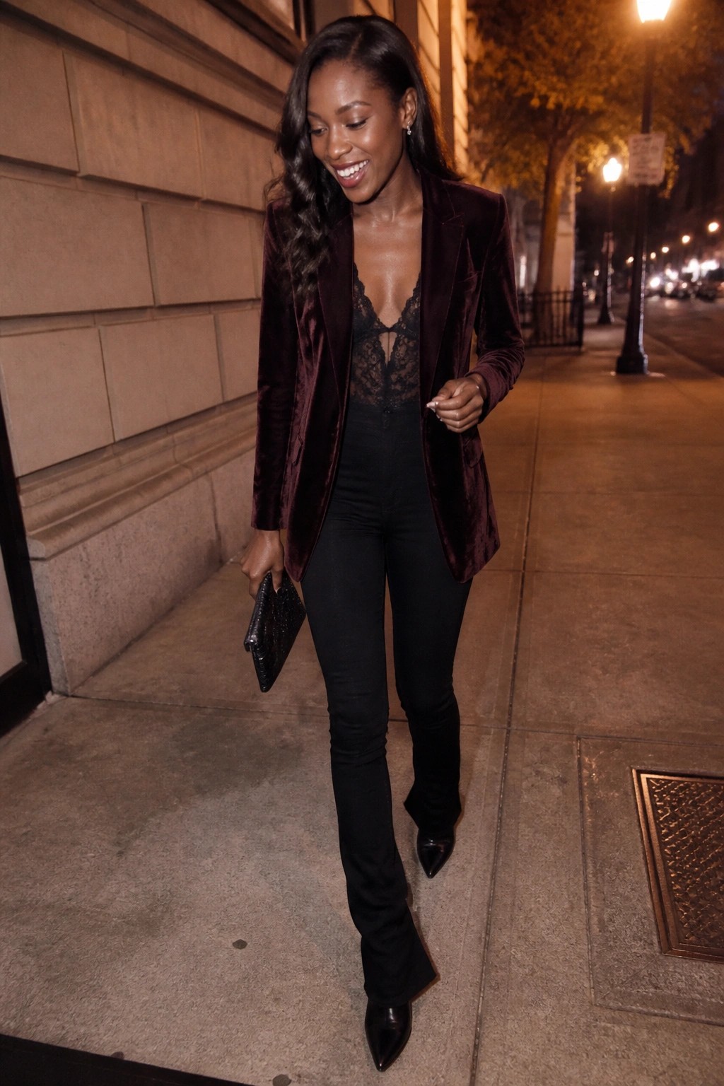 Woman in burgundy velvet blazer over black lace bodysuit on nighttime sidewalk.