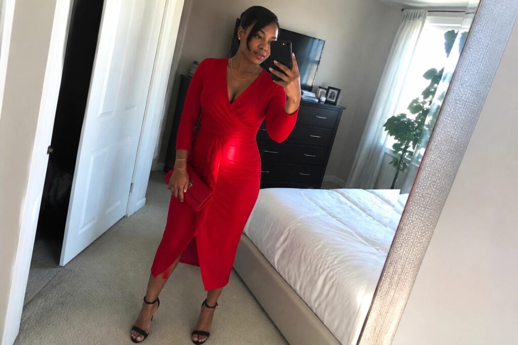 Woman in red long-sleeved wrap dress taking mirror selfie in bedroom