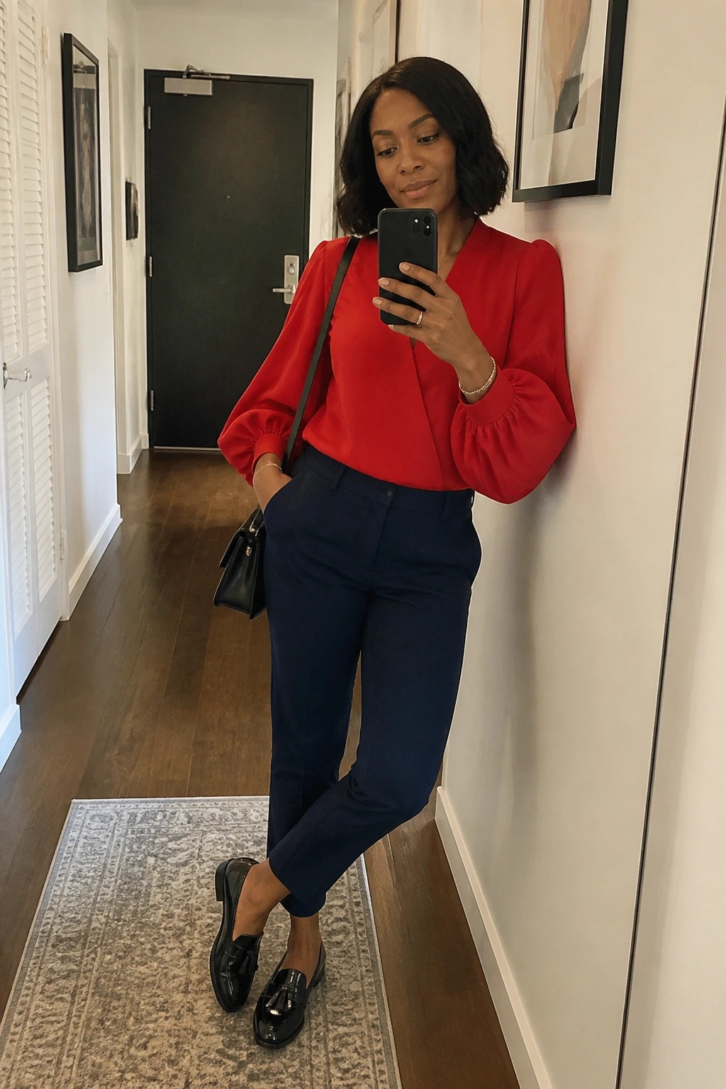 Woman in red puff-sleeve blouse and navy pants taking mirror selfie in hallway