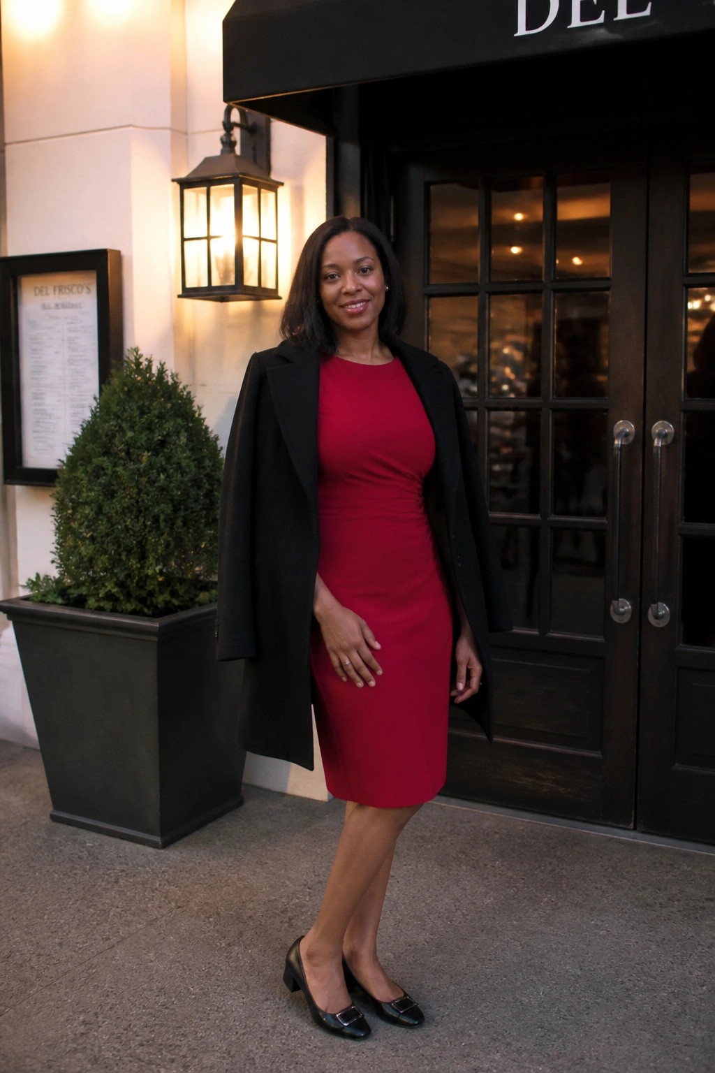 Woman in red dress and black coat outside Del Frisco's restaurant entrance.