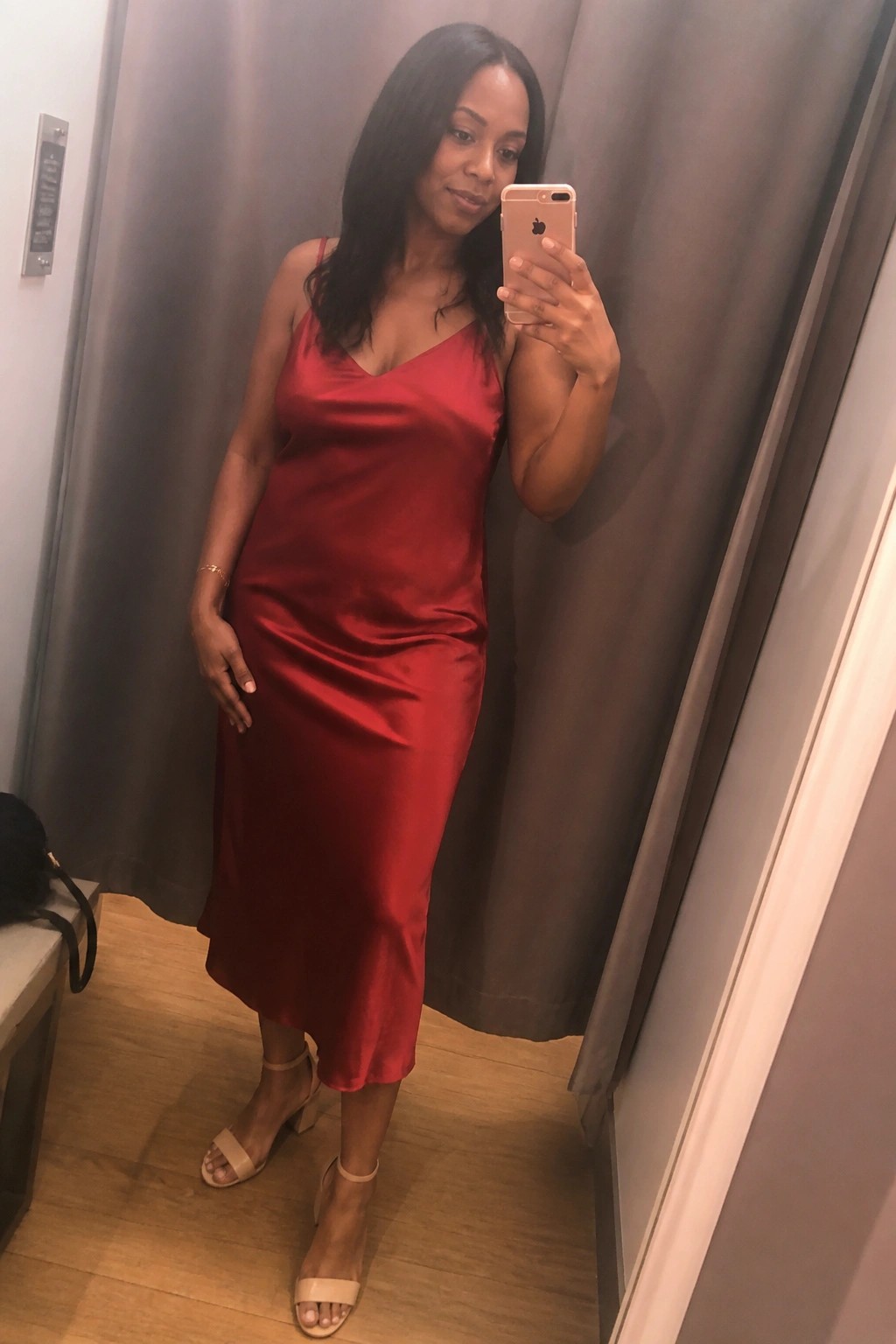 Woman in red satin midi dress takes mirror selfie wearing beige heels in fitting room