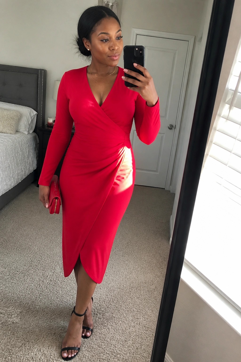 Woman in red long-sleeved wrap dress taking mirror selfie in bedroom