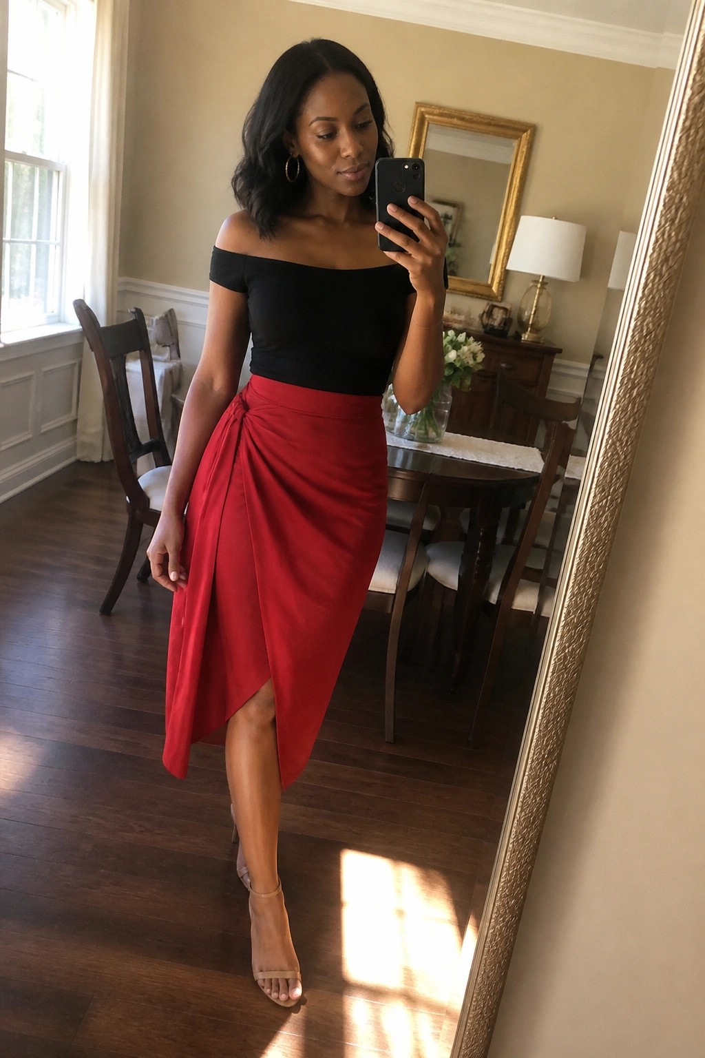 Woman in black off-shoulder top and red wrap skirt taking mirror selfie in dining room