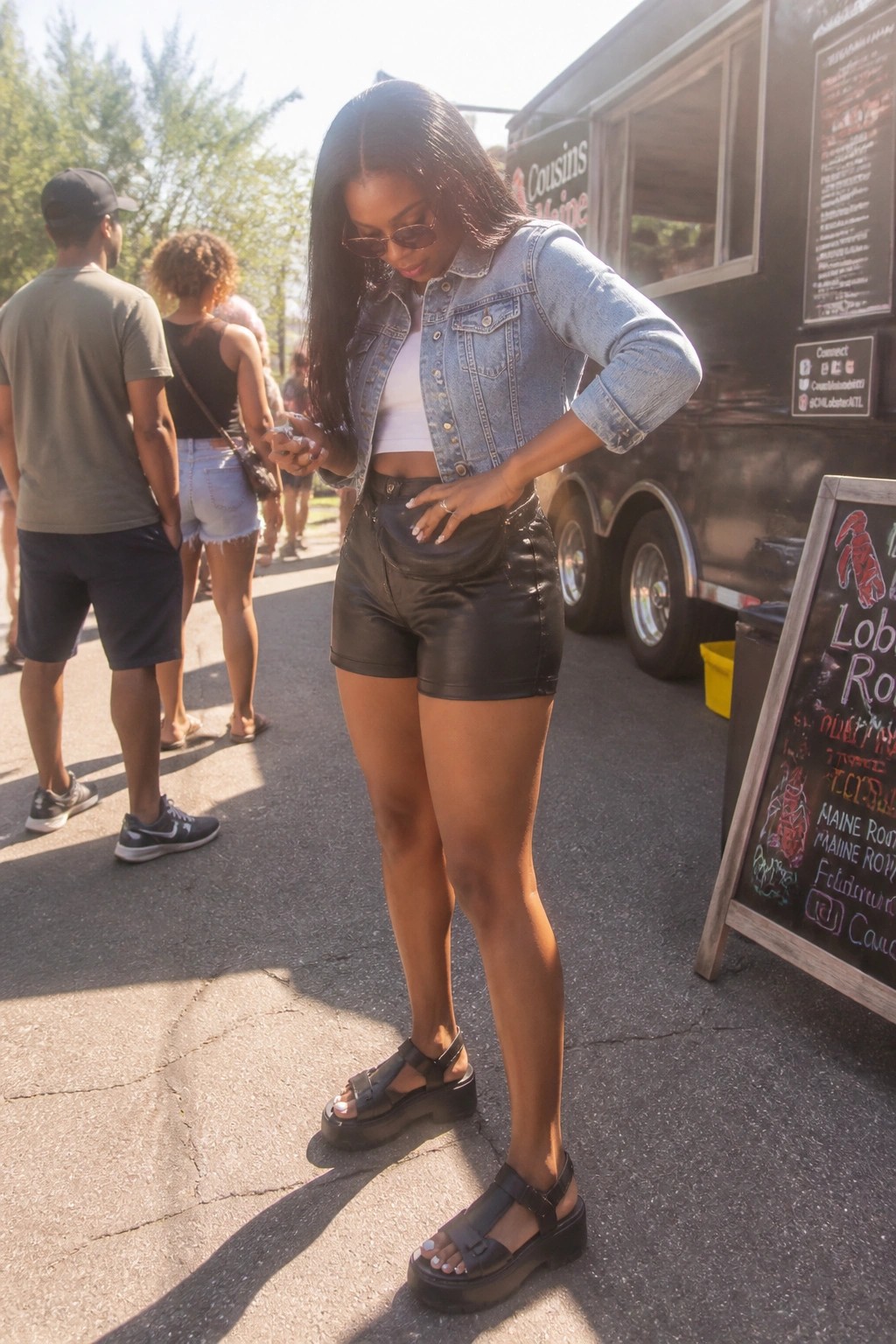 Woman in denim jacket and leather shorts checks phone by food truck