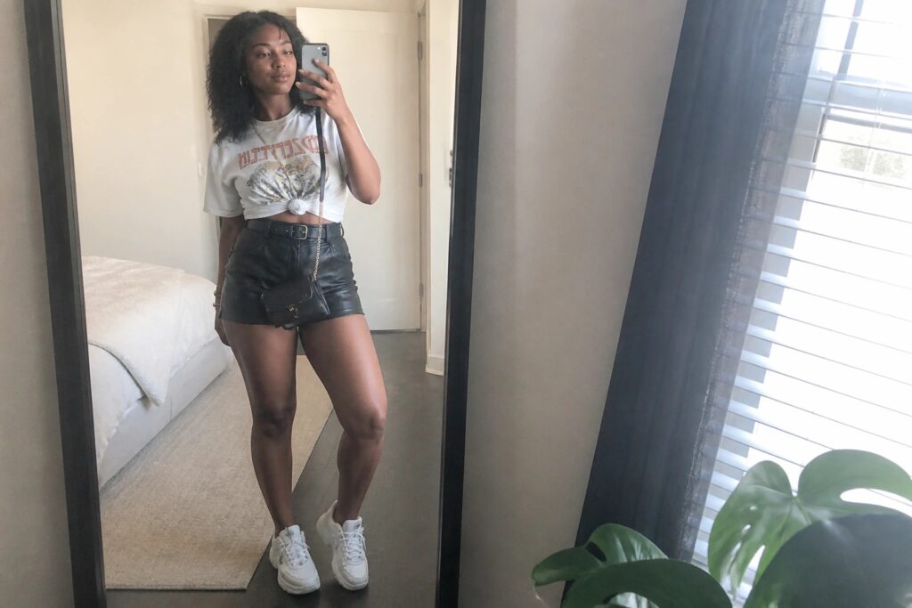 24 Stylish Leather Shorts Concert Outfit Ideas for Black Women That Keep You Comfortable Woman in white graphic tee and black leather shorts taking bedroom mirror selfie