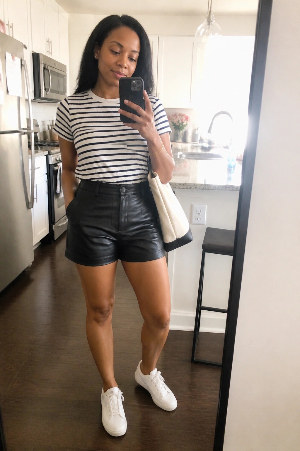 Woman in striped shirt and black leather shorts taking kitchen mirror selfie