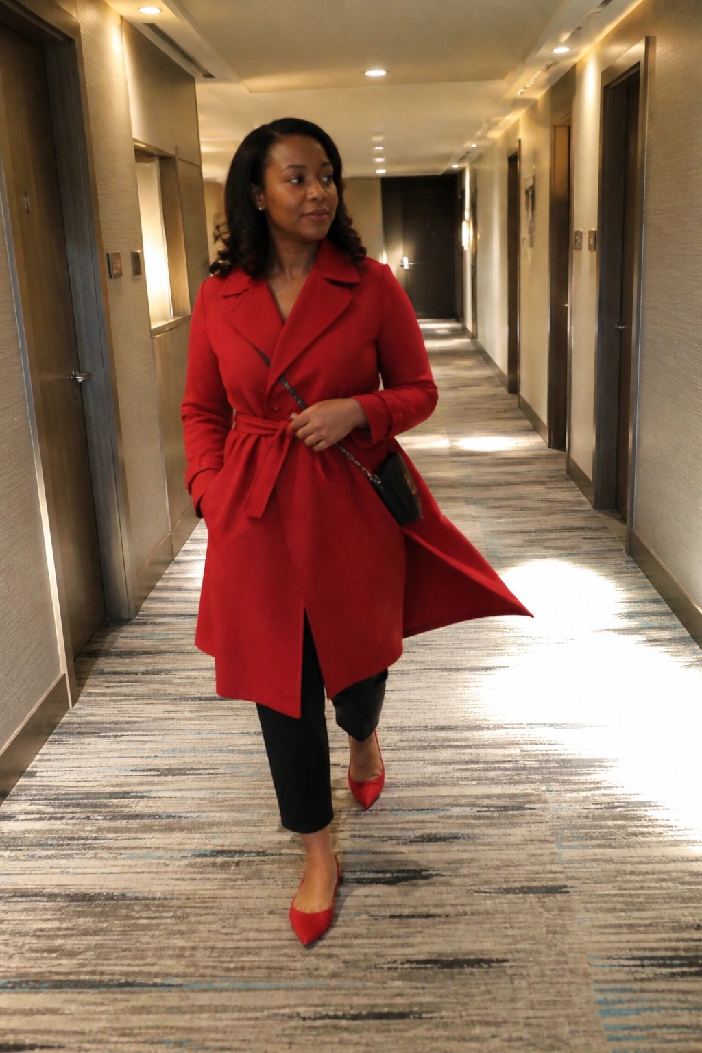 Woman in red coat and heels walks down hotel hallway
