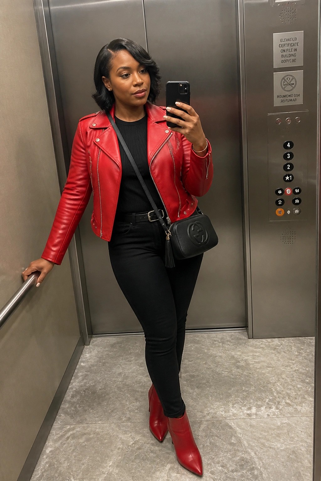 Woman in red leather jacket and boots taking selfie in elevator with black handbag