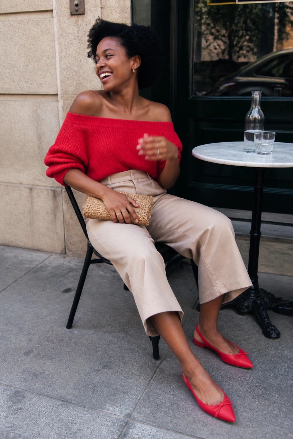 Smiling woman in red off-shoulder sweater and beige pants at outdoor cafe table