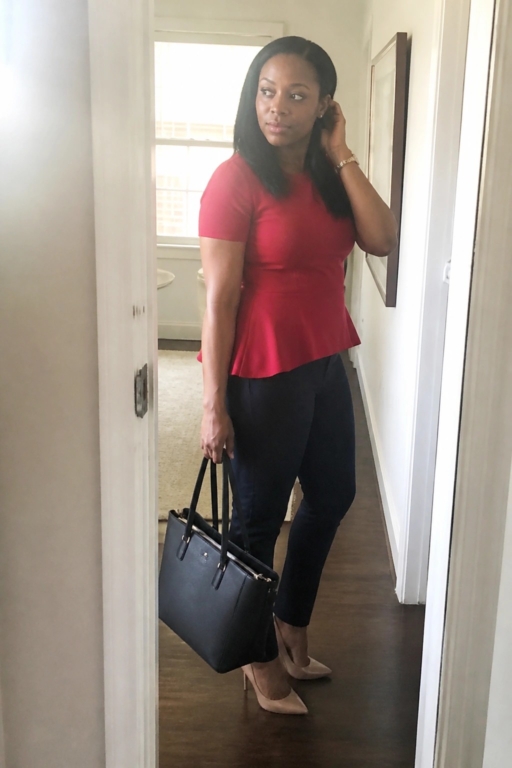 Woman in red peplum top and navy pants holding black handbag in hallway