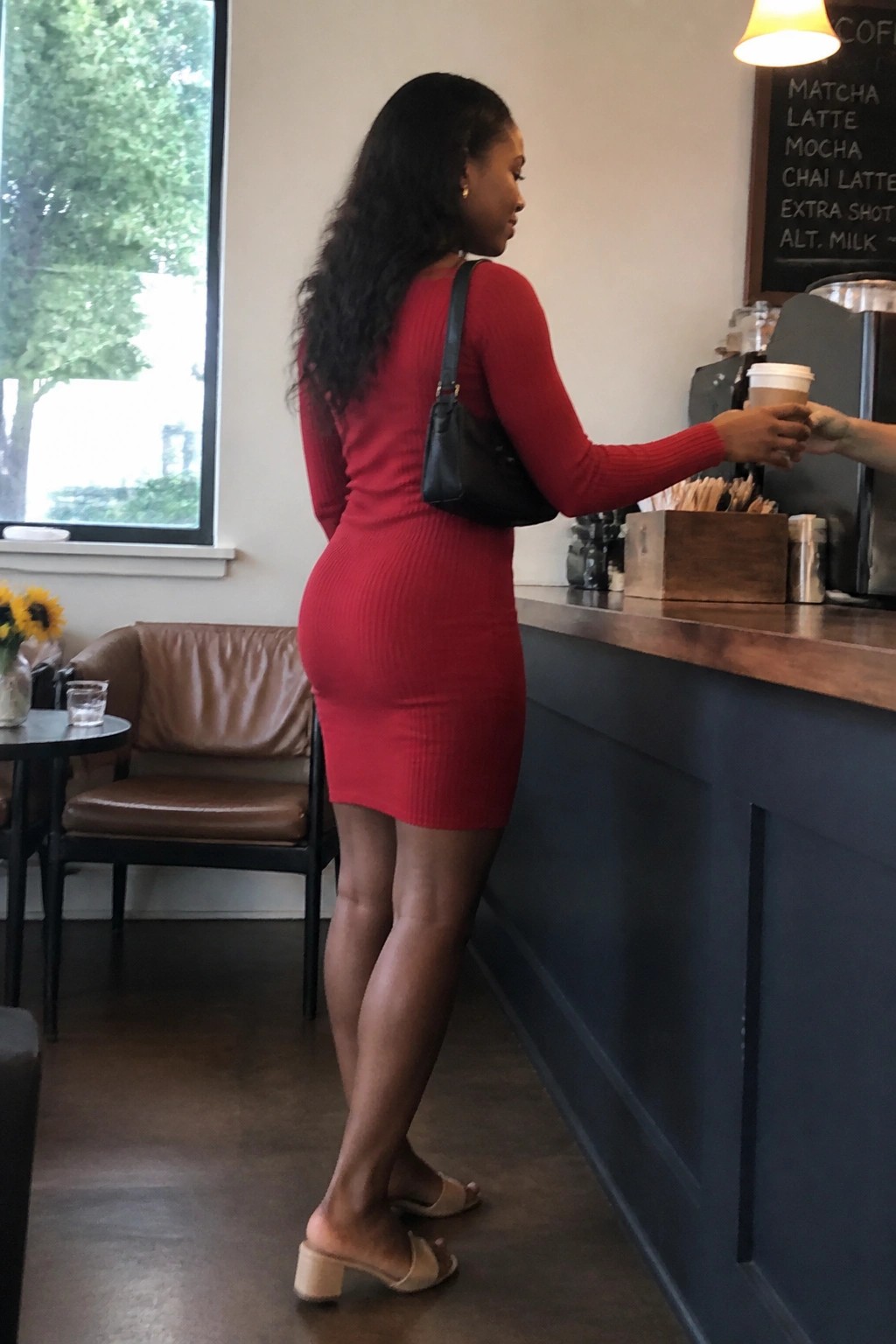 Woman in red ribbed dress receiving coffee at wooden cafe counter with black bag
