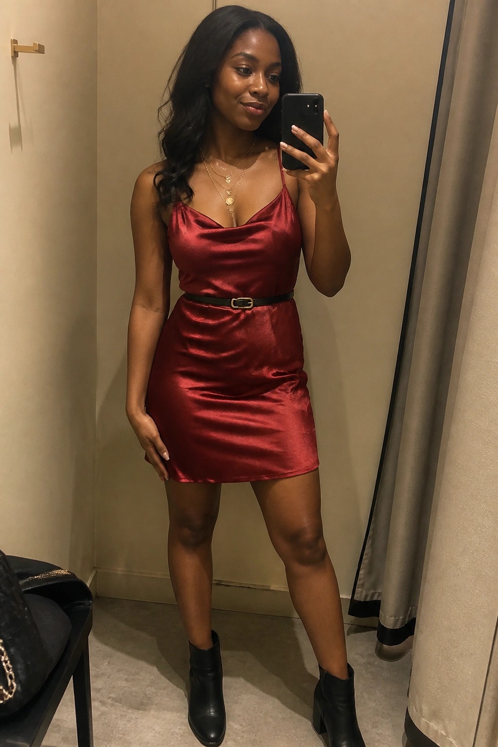 Woman in red satin mini dress with black belt taking mirror selfie in boots