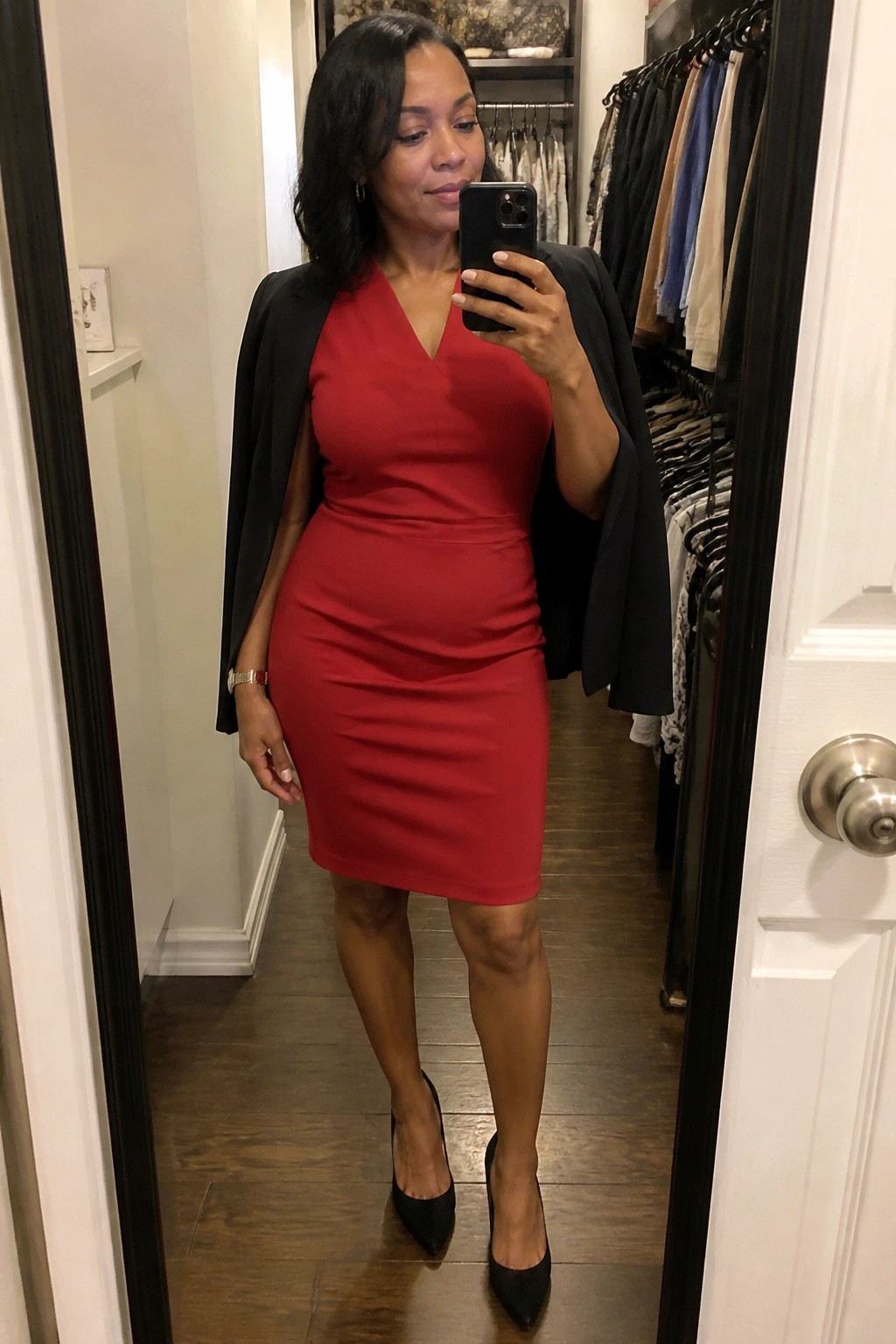 Woman in red dress and black blazer taking mirror selfie in hallway
