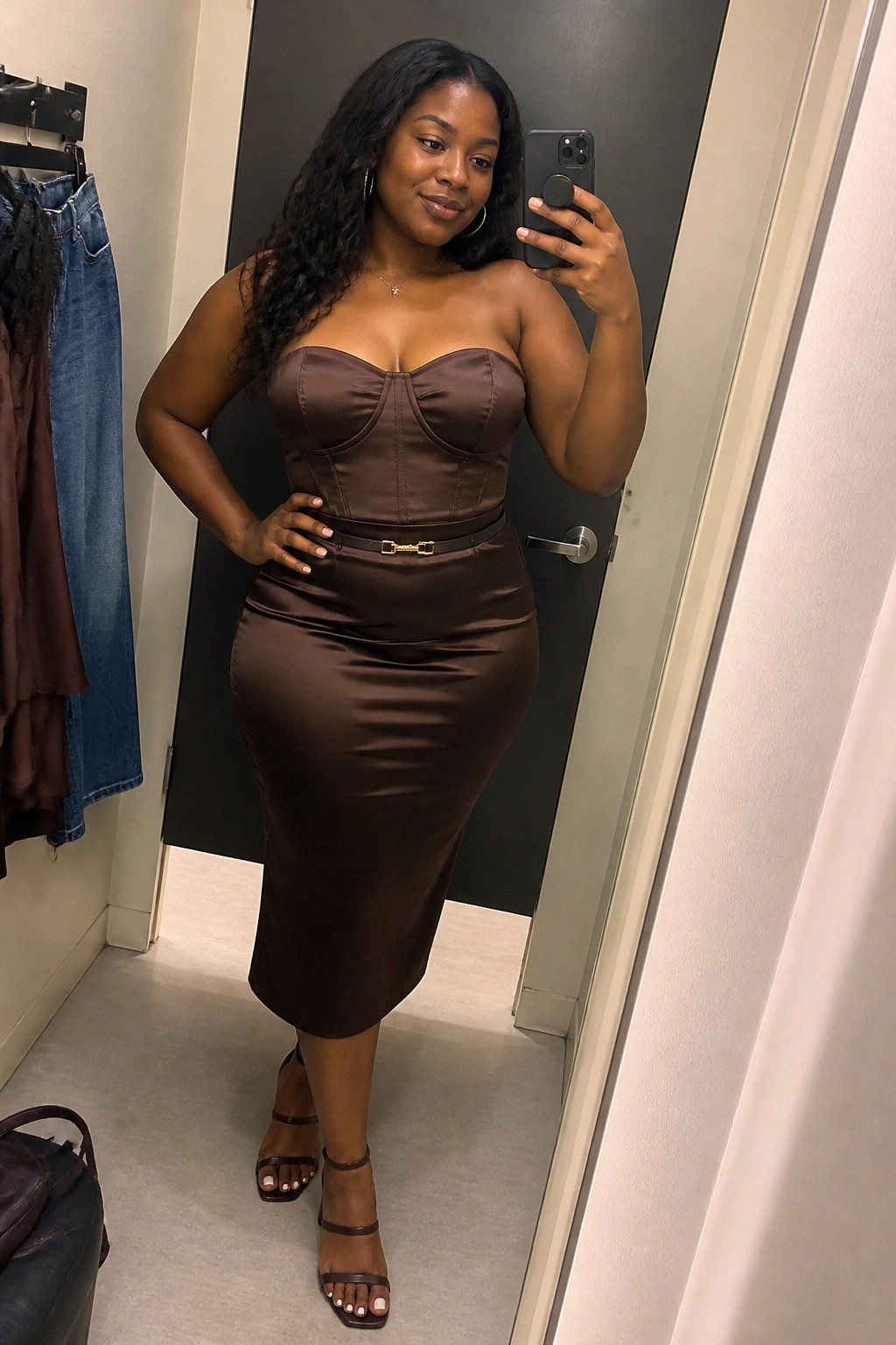 Plus size Black woman wearing a brown satin corset top with matching midi skirt, thin belt, and strappy heels in a mirror selfie.