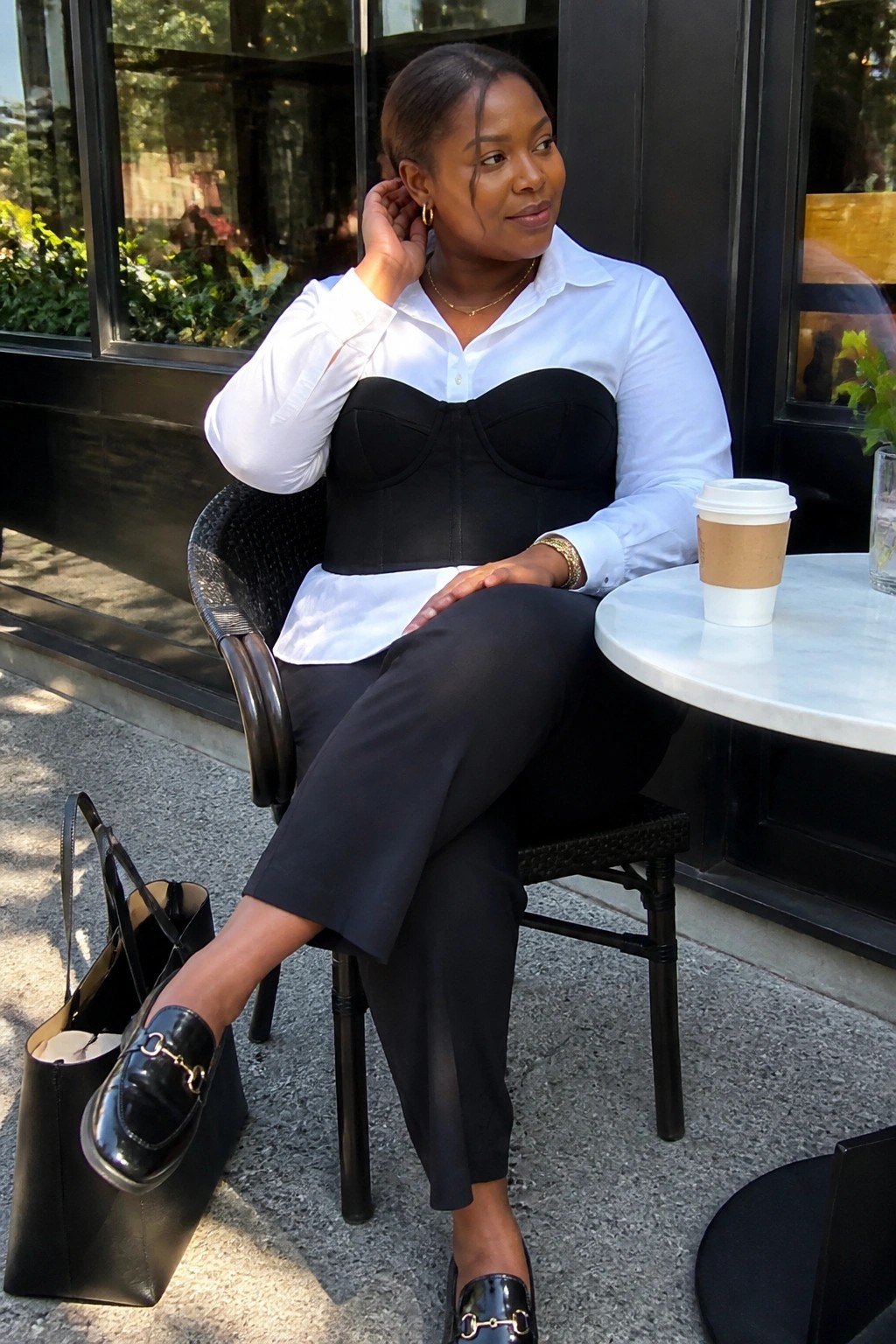 Woman in white shirt and black corset at outdoor cafe with coffee and bag.