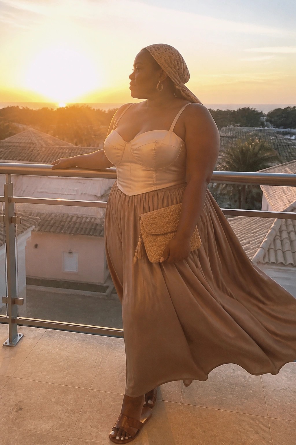 Woman in beige corset top and flowing skirt on balcony at sunset