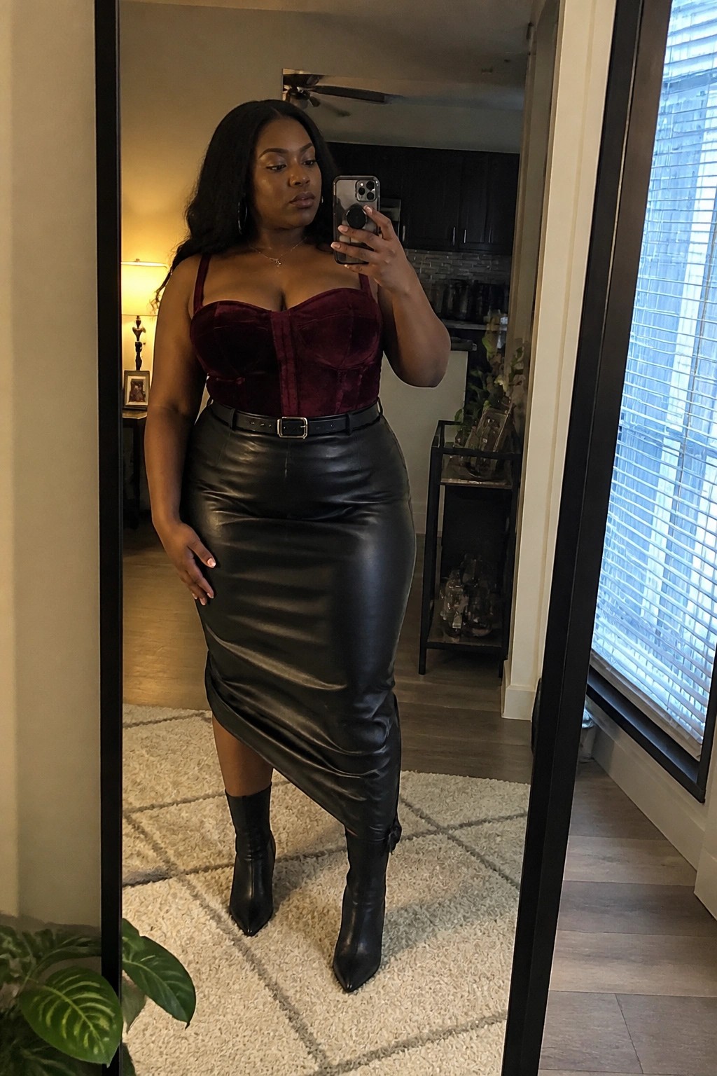 Woman in maroon velvet corset and black leather skirt taking mirror selfie with phone