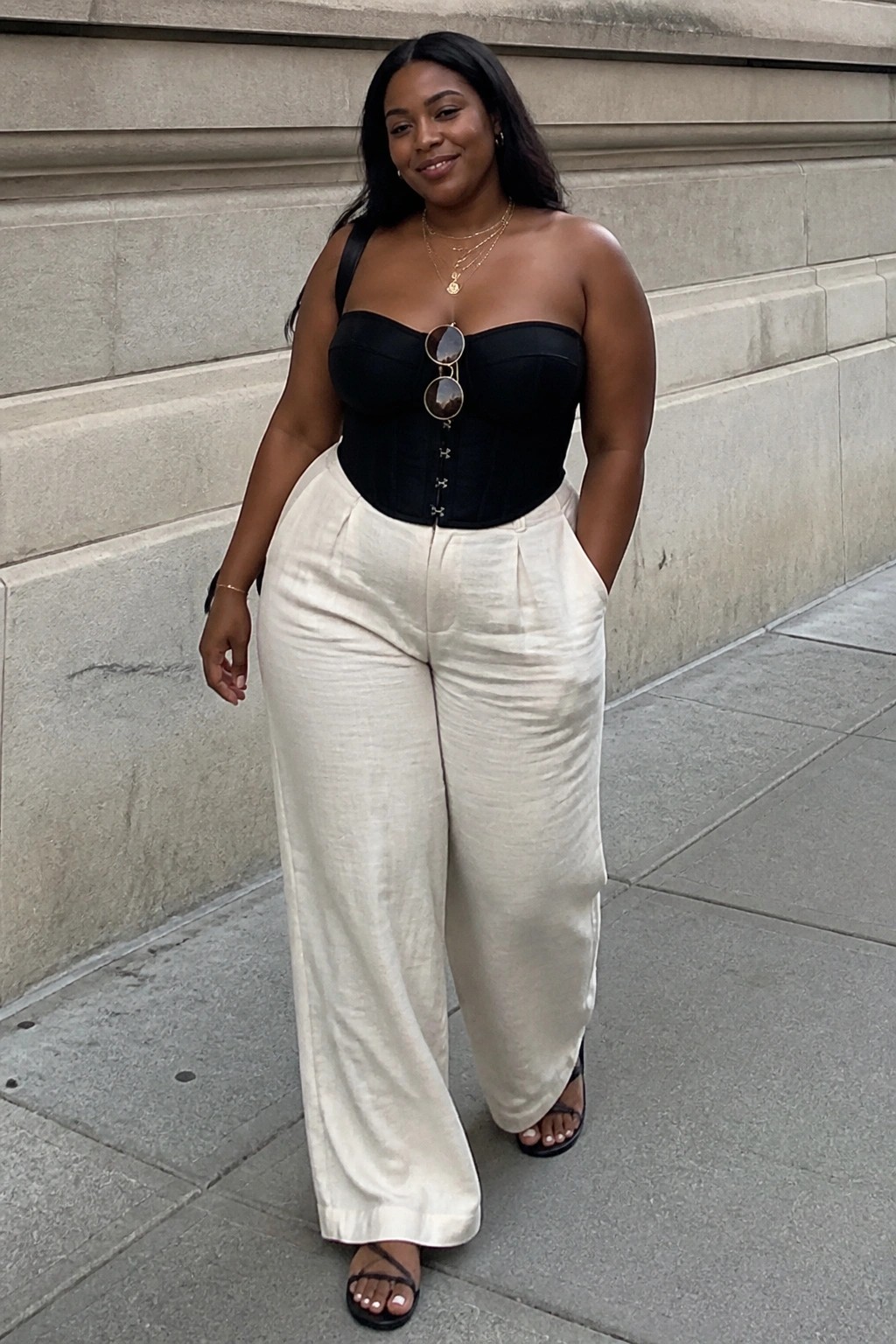 Woman in black strapless corset and white wide-leg pants on city sidewalk