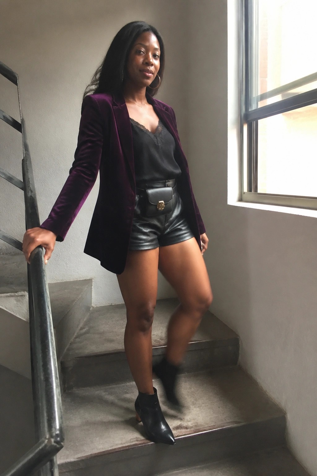 Woman in purple velvet blazer, black lace top, and leather shorts on stairs.