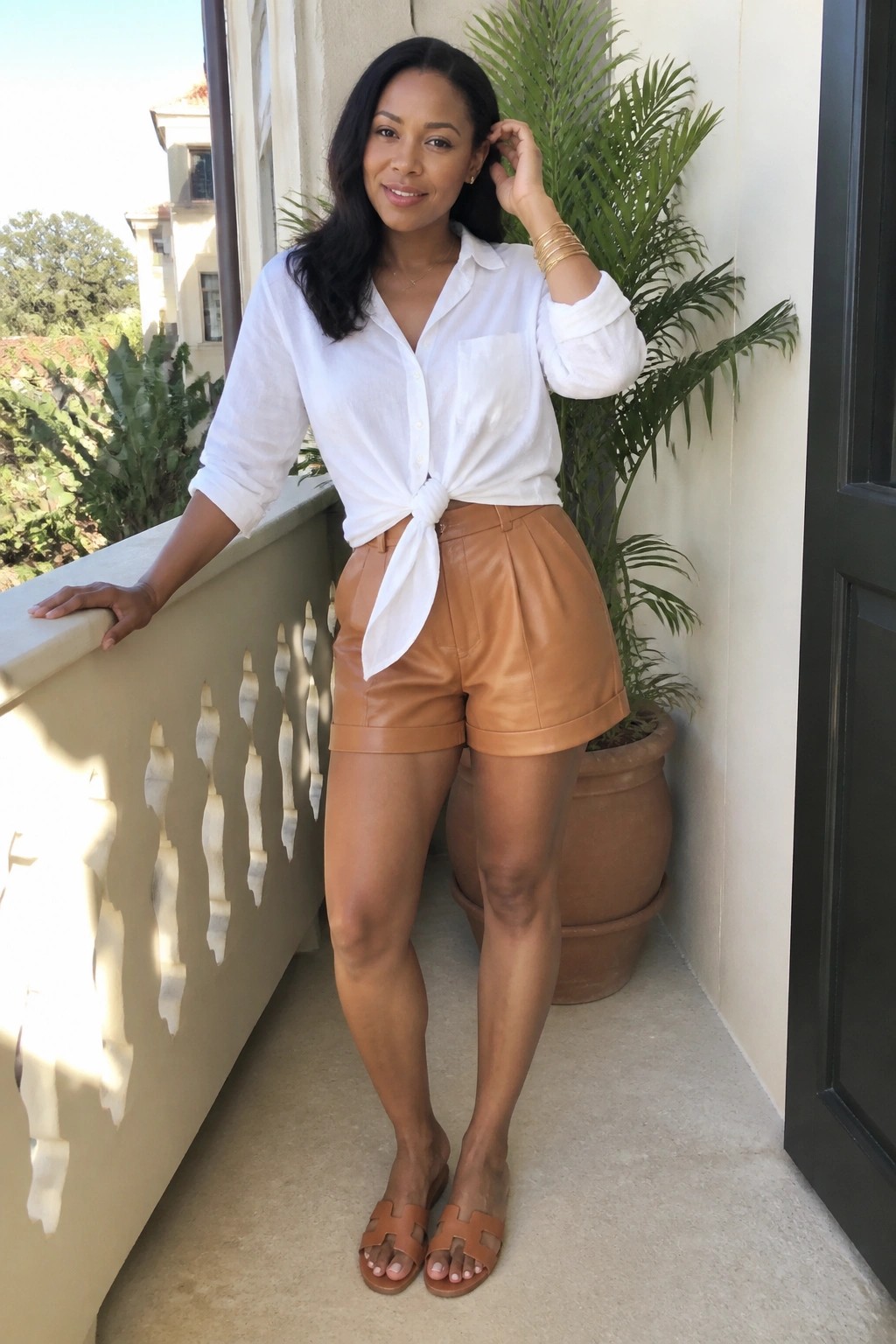 Woman in white tied shirt and brown leather shorts on sunny balcony