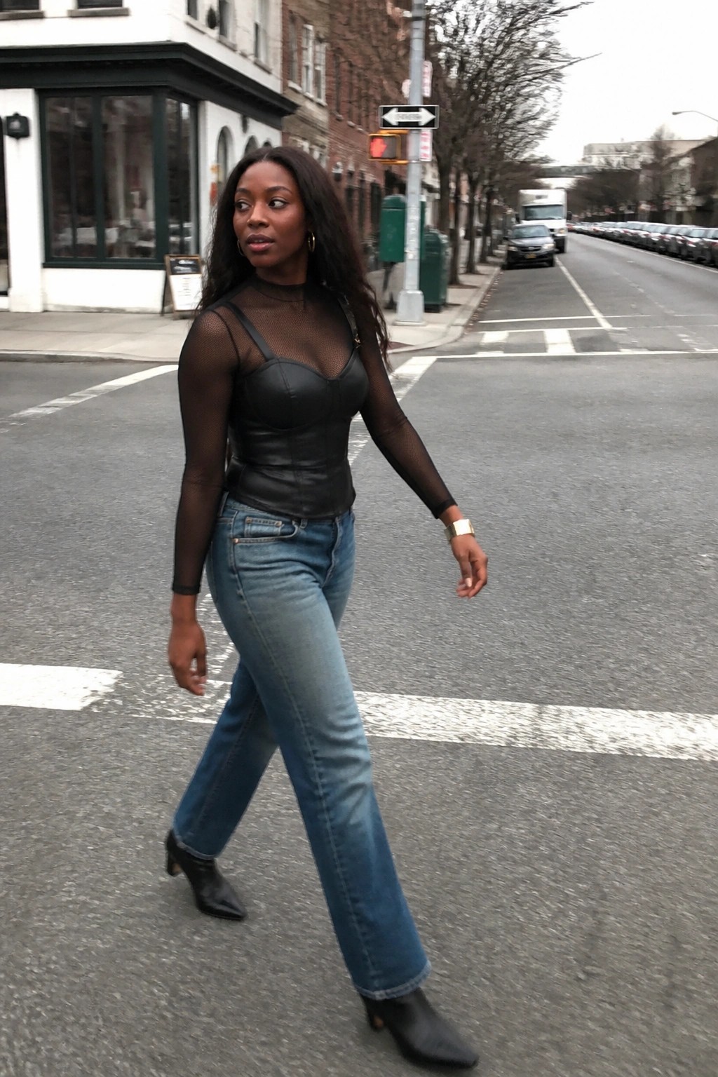 Woman in sheer black mesh top and leather corset with blue jeans crossing city street