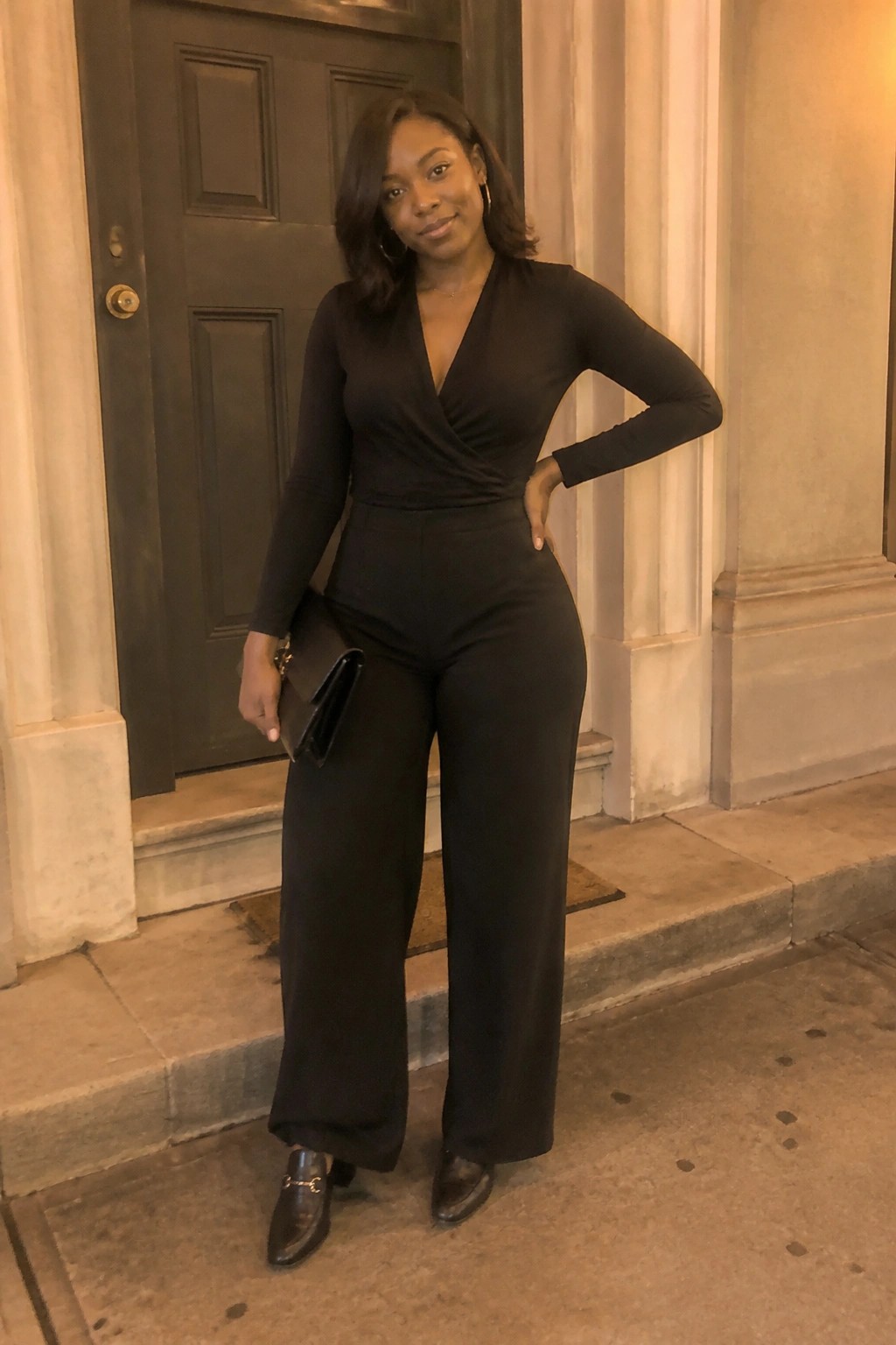 Woman in black wrap top and wide-leg pants holding clutch on steps
