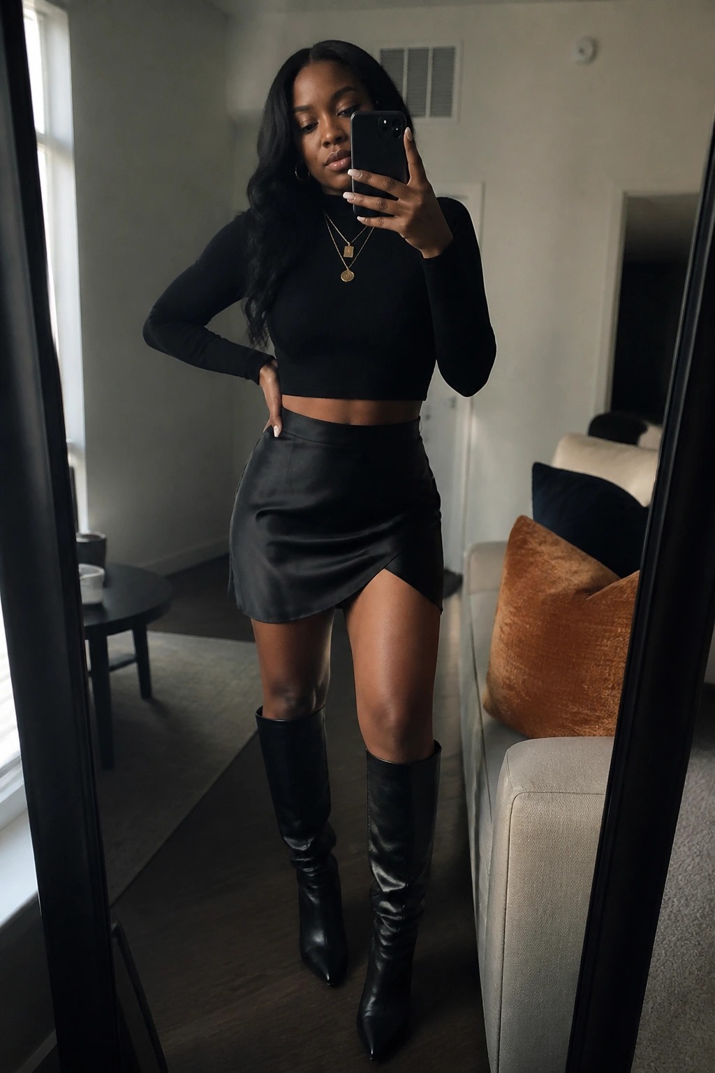Woman taking mirror selfie in black crop top, leather skirt, and boots