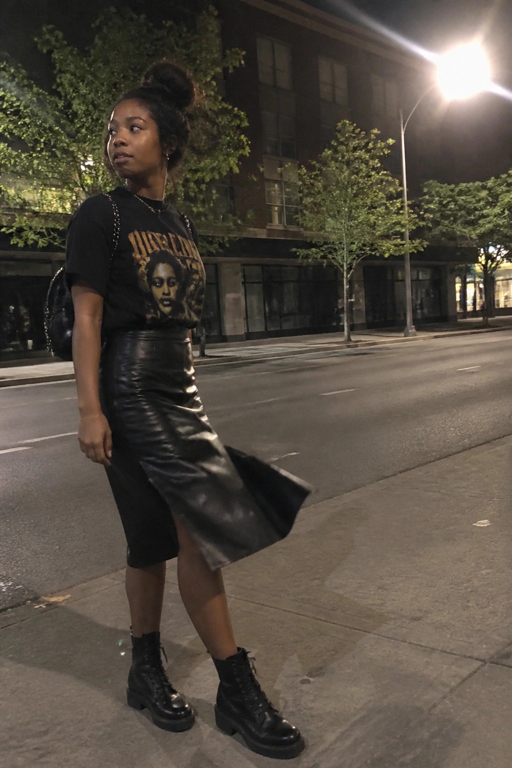 Woman in black graphic tee and flowing leather skirt on nighttime city street.
