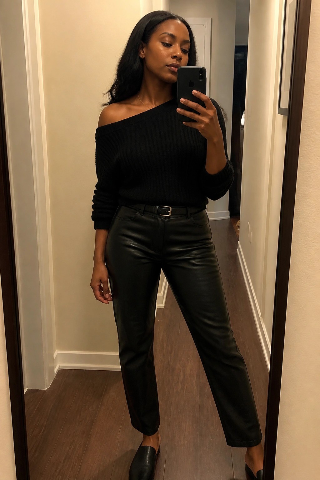 Woman in black off-shoulder sweater and leather pants taking mirror selfie with phone