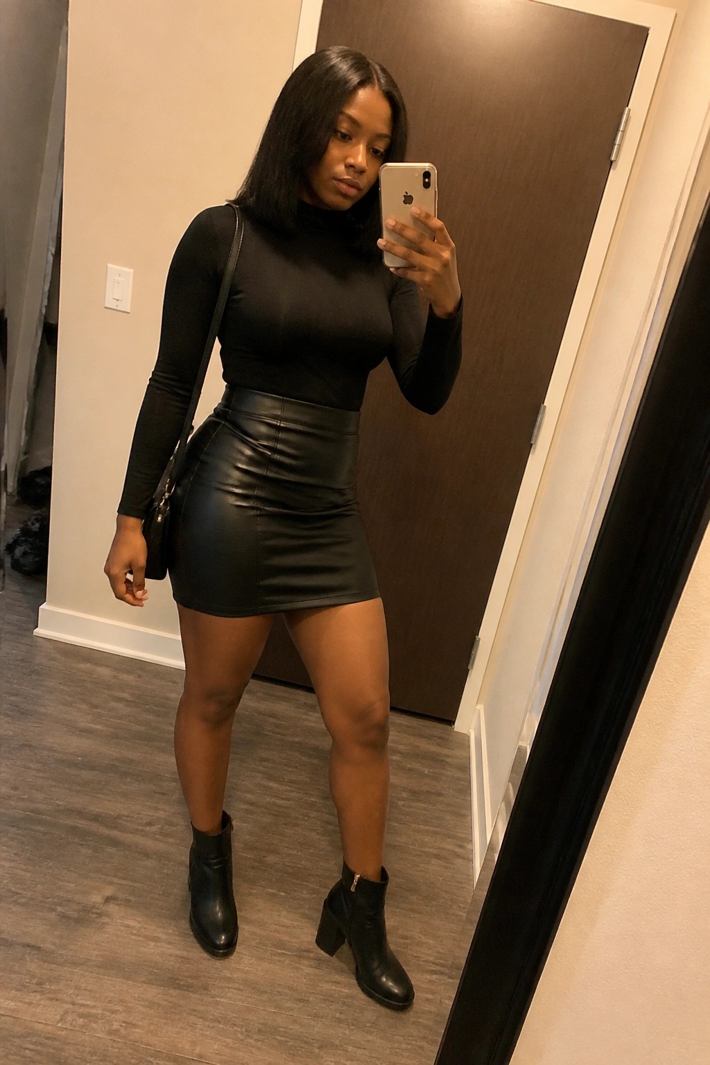 Woman in black turtleneck and leather skirt taking mirror selfie with phone