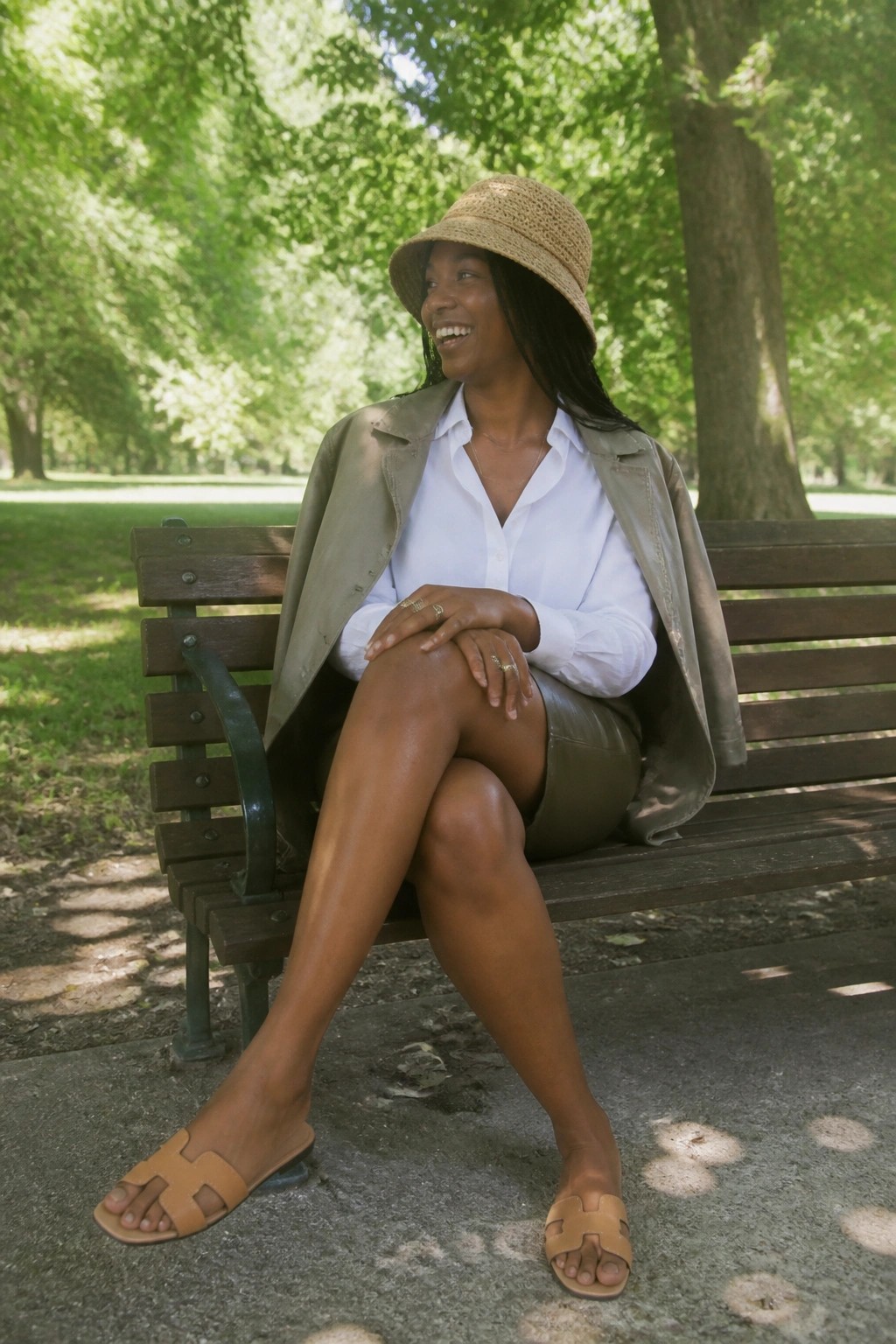 Woman in straw hat and white blouse smiling on wooden park bench